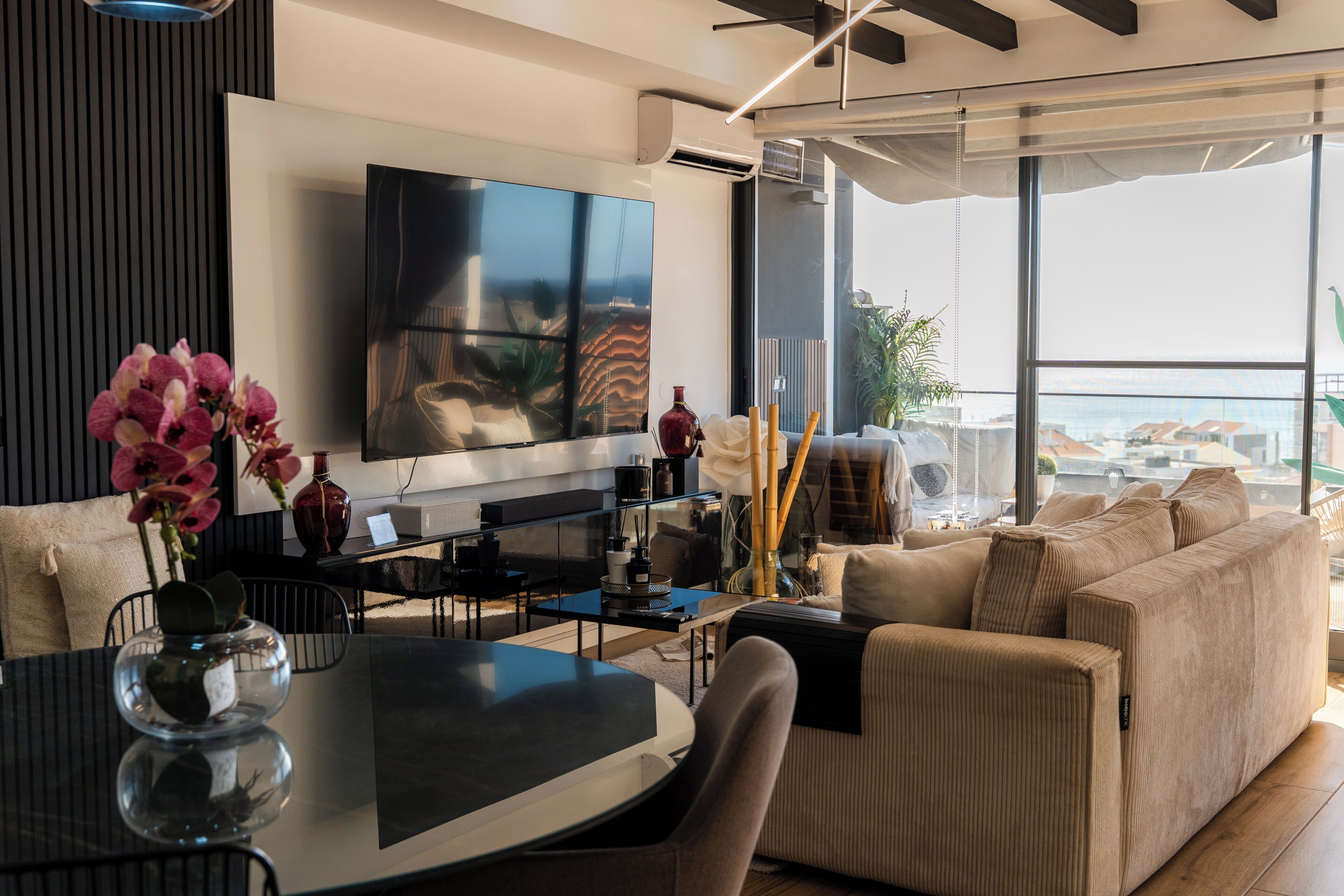A modern living room with a flat-screen TV, a dining table, and a sofa.