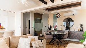 A modern living room with a sofa, dining table, and chairs. There is a kitchen area with a dining table and chairs, and a large mirror on the wall.