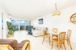 A modern living room with a glass dining table, comfortable seating, and a view of the ocean.