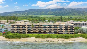 A multi-story hotel with balconies, located near a beach with waves.