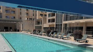A swimming pool with lounge chairs and a covered area, surrounded by multi-story buildings.