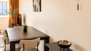 Un comedor con una mesa de madera, sillas y un banco negro. Hay un reloj de pared y una obra de arte enmarcada sobre la mesa.