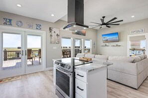 A modern kitchen with a built-in stove, a ceiling fan, and a large window overlooking a deck. - The Blue Crab - On Canal, boat slip w/lift, Bay access, outdoor bar (Gilchrist)