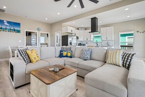 A modern living room with a sectional sofa, a coffee table, and a kitchen in the background. - The Blue Crab - On Canal, boat slip w/lift, Bay access, outdoor bar (Gilchrist)