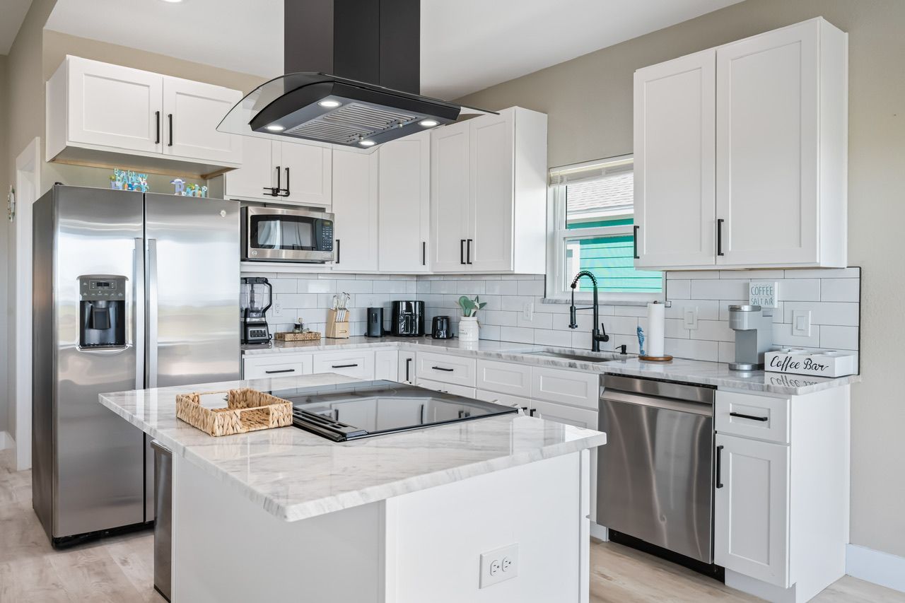 Una cocina moderna con gabinetes blancos, electrodomésticos de acero inoxidable, una isla central y una barra para café.