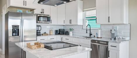 Una cocina moderna con gabinetes blancos, electrodomésticos de acero inoxidable, una isla central y una barra para café.