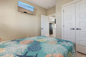 A bedroom with a bed, a television on the wall, and a door leading to another room. - The Blue Crab - On Canal, boat slip w/lift, Bay access, outdoor bar (Gilchrist)