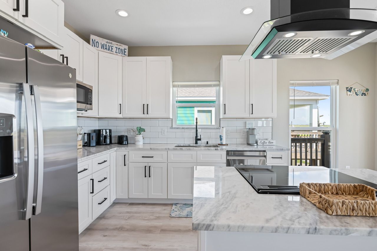 A modern kitchen with white cabinetry, stainless steel appliances, and a marble countertop.