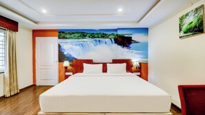 A hotel room with a large bed, a nightstand with a lamp, a door, and a wall mural of a waterfall. - Gardeenia Comfortes  (Bommasandra)