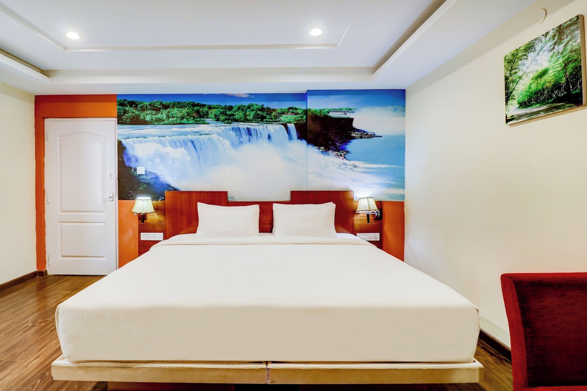 A hotel room with a large bed, a nightstand with a lamp, a door, and a wall mural of a waterfall.