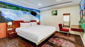 A hotel room with a large bed, a desk, a chair, a mirror, and a wall mural of a waterfall. - Gardeenia Comfortes  (Bommasandra)