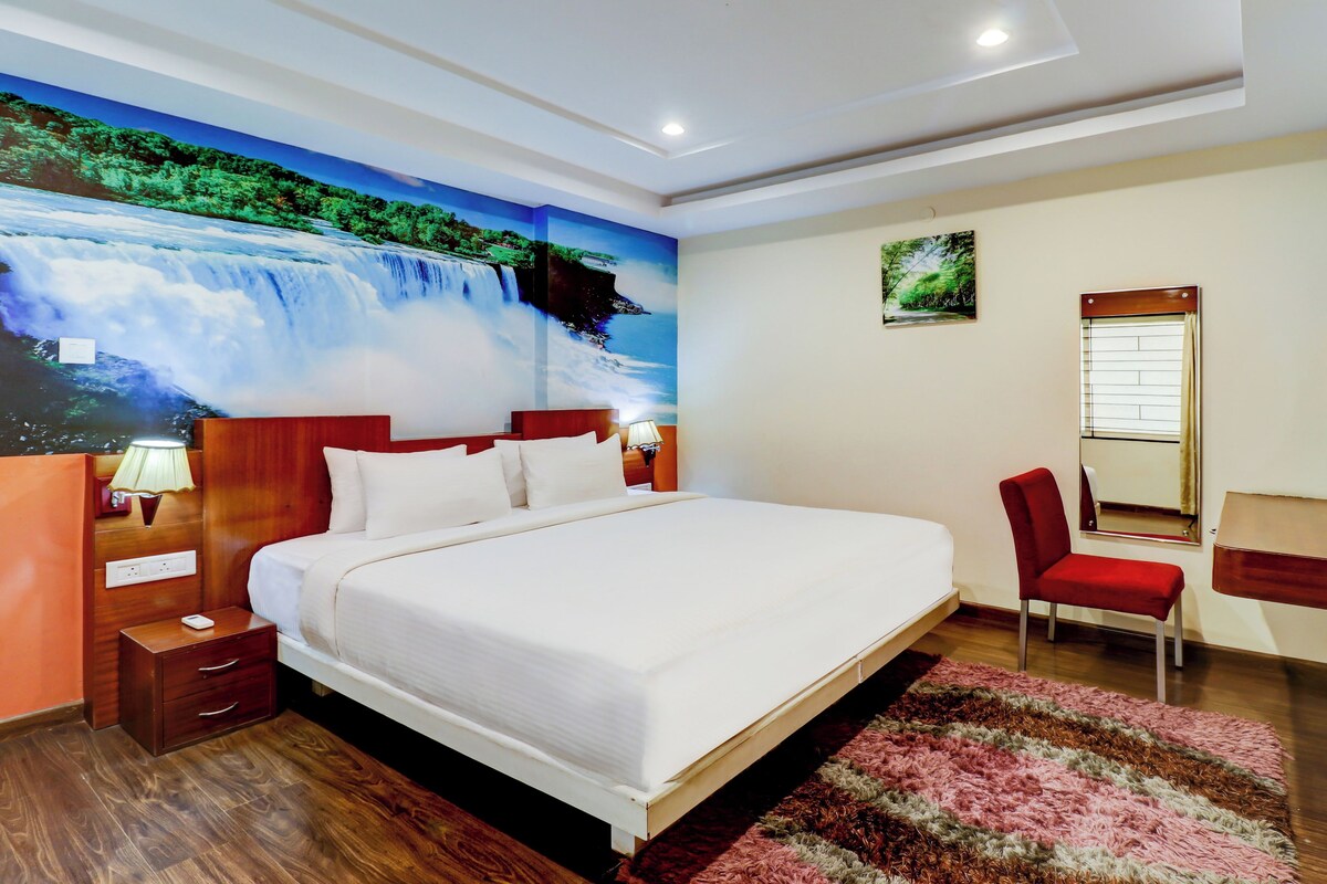 A hotel room with a large bed, a desk, a chair, a mirror, and a wall mural of a waterfall.