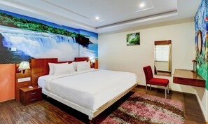 Ein Hotelzimmer mit einem großen Bett, einem Schreibtisch, einem Sessel, einem Spiegel und einem Wandbild einer Wasserfälle.