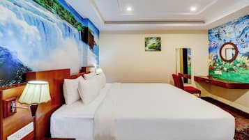 Una habitación de hotel con una cama grande, una mesita de noche con lámpara, un escritorio con espejo y un mural en la pared que representa una cascada.