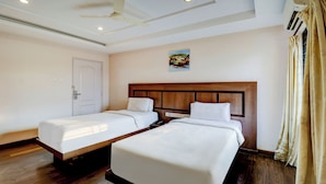 Una habitación de hotel con dos camas individuales, un ventilador de techo, un equipo de aire acondicionado y un cuadro en la pared.