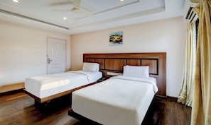 Una habitación de hotel con dos camas individuales, un ventilador de techo, un equipo de aire acondicionado y un cuadro en la pared.