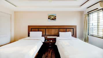 A hotel room with two beds, a wooden headboard, a painting on the wall, and a window with curtains.