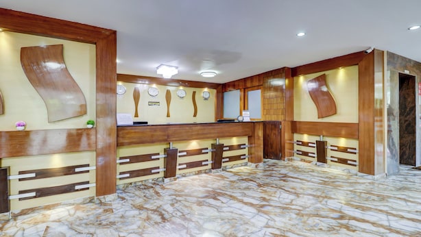 Un área de recepción con piso de mármol, mostrador de madera y relojes en la pared.