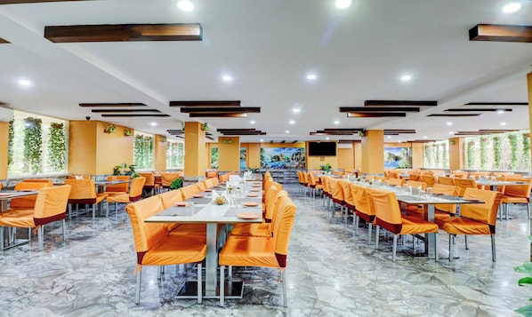 A spacious dining area with multiple tables and chairs, a marble floor, and a large mural on the wall. - Gardeenia Comfortes (Anekal)