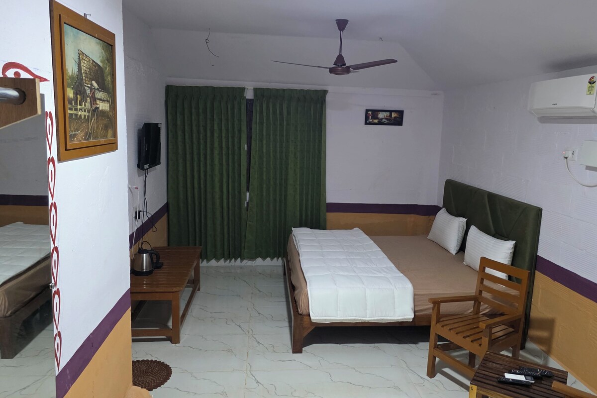 A hotel room with two beds, a ceiling fan, an air conditioning unit, a television, and a small table with a kettle.