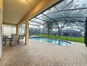 A covered outdoor swimming pool area with a brick floor, glass enclosure, and seating. - PROMO Magical 6 BR Villa, Pool/Spa, Windsor Hills - by Blue Sky Villas (Kissimmee)