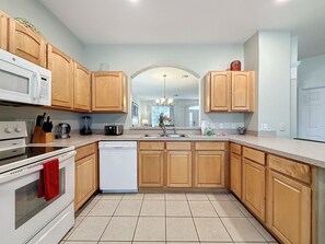 A modern kitchen with wooden cabinets, a white dishwasher, a stove, and a microwave. - PROMO Magical 6 BR Villa, Pool/Spa, Windsor Hills - by Blue Sky Villas (Kissimmee)
