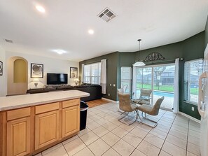 A modern kitchen with a central island, a dining area with a glass table, and a living room with a sofa and TV. - PROMO Magical 6 BR Villa, Pool/Spa, Windsor Hills - by Blue Sky Villas (Kissimmee)