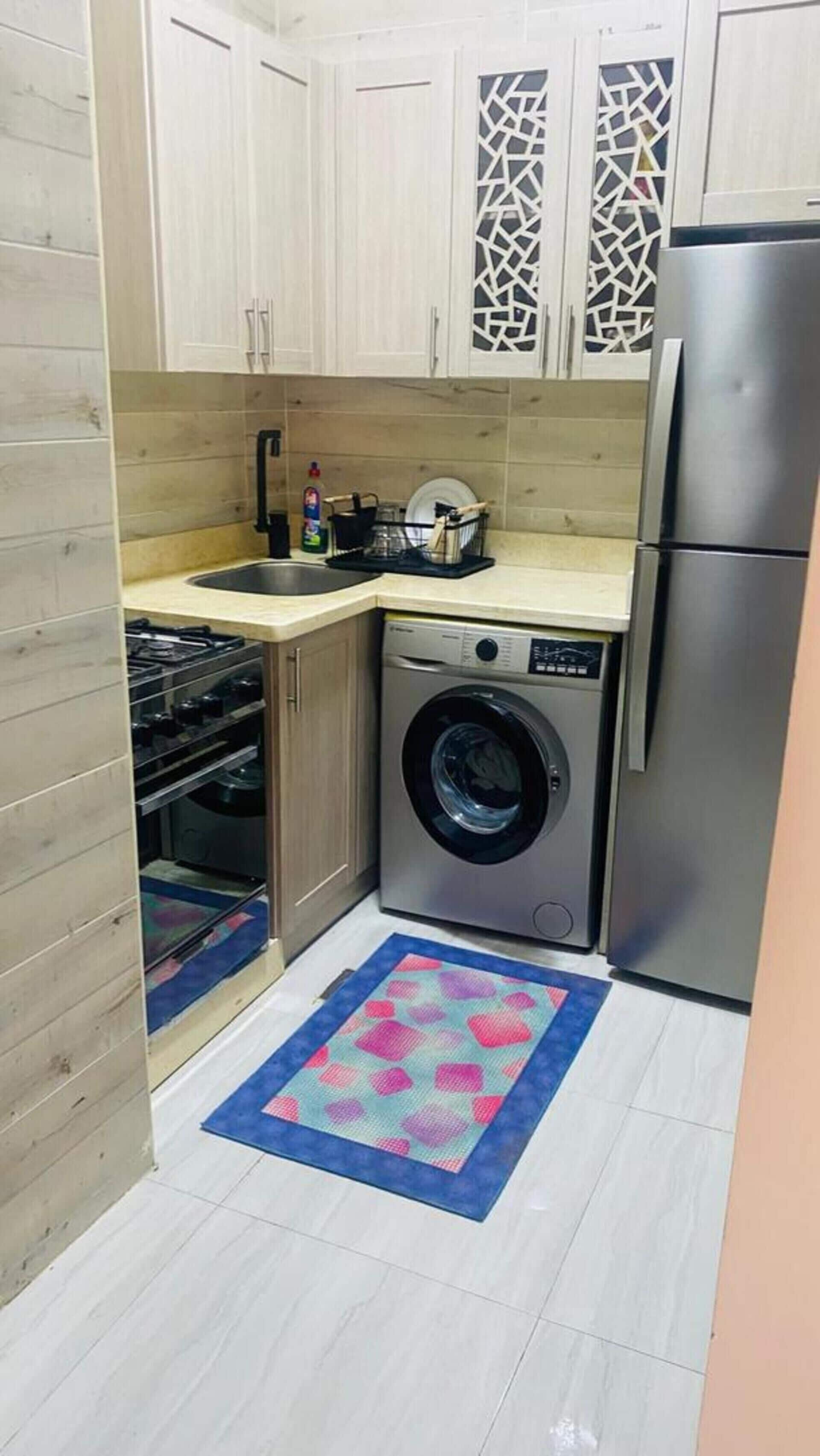 Een praktische keuken met een ingebouwde wasmachine en droger, een roestvrijstalen koelkast en een klein spoelgedeelte.