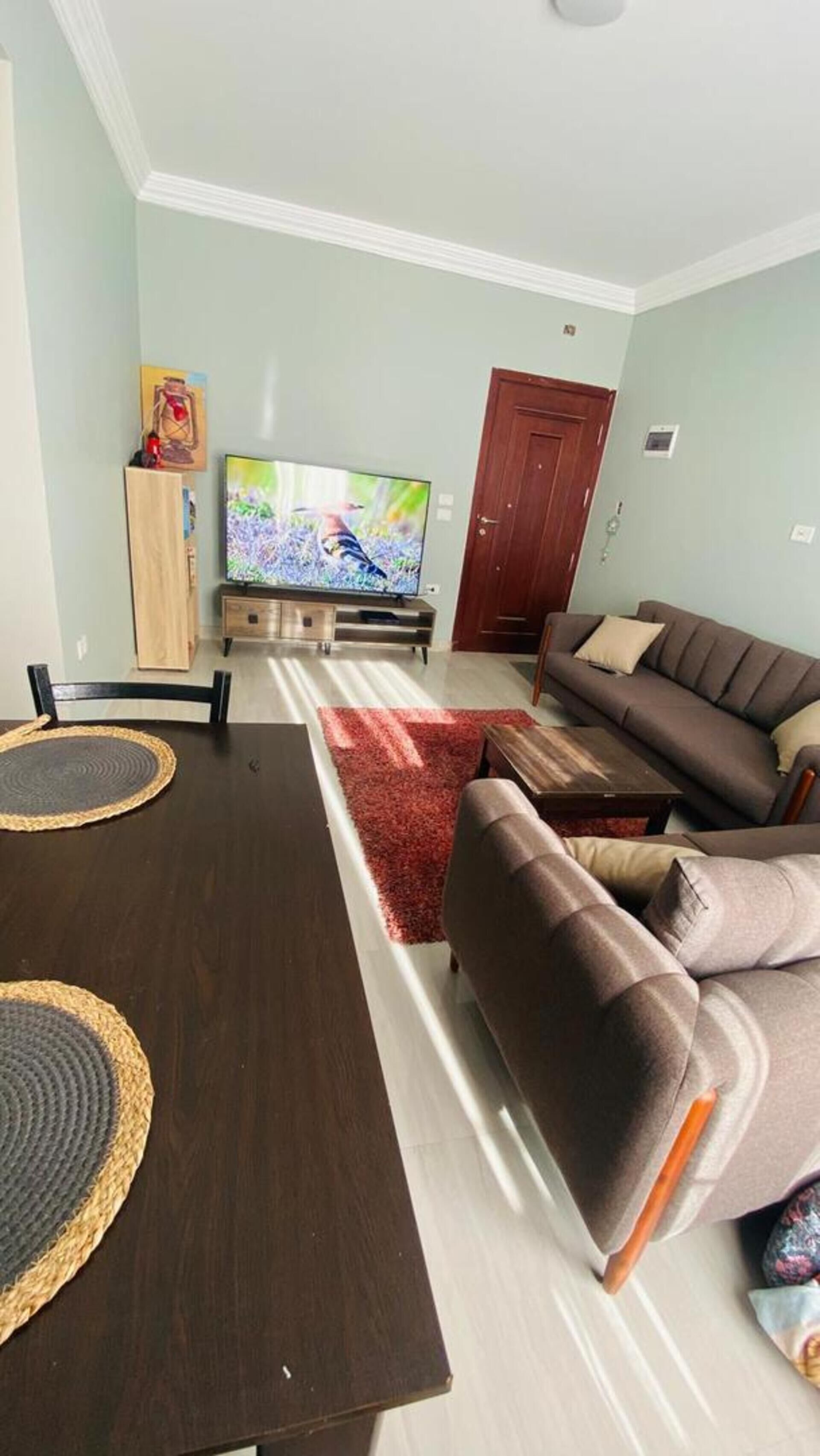 Een woonkamer met een donker houten eettafel, twee banken, een televisie en een rood vloerkleed.