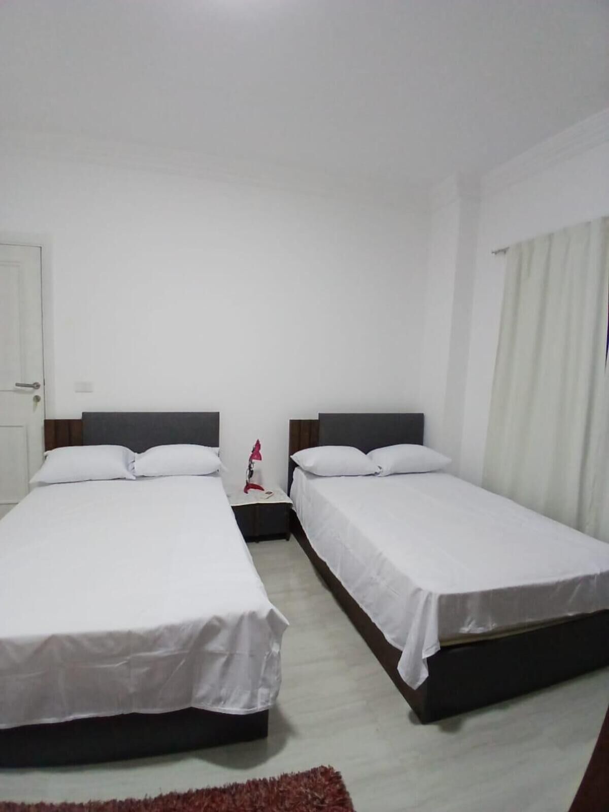 Una camera d'albergo con due letti singoli, un comodino, una lampada e una porta.