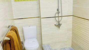 Een compacte badkamer met toilet, douche en een handdoekrek met handdoeken.