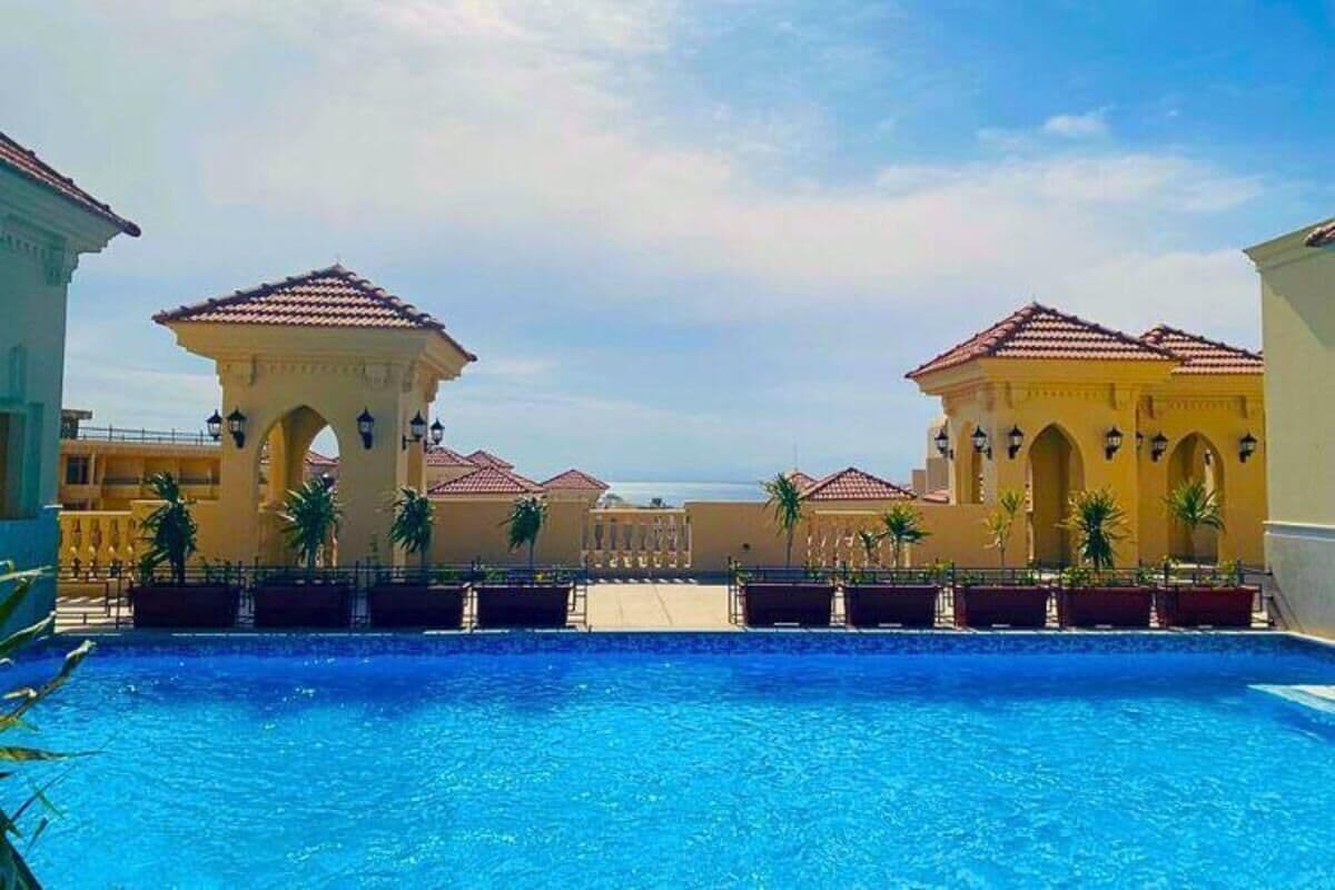 A swimming pool with a clear view of a building with arches and a tiled roof.
