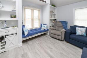 A modern living room with a built-in bench, a grey armchair, a blue sofa, and a white cabinet with shelves. - 3 BR, Walk to the Beach Townhouse in Surfside Beach! Sandy Sea (Surfside Beach)
