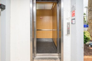An elevator with a metal door, a wooden interior, and a control panel with emergency contact information. - 2BR Oceanfront Condo with Elevator and Shared Pool! South Shores II 203 (Surfside Beach)
