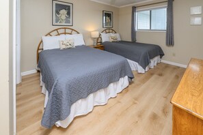 Een slaapkamer met twee bedden, een houten vloer, een nachtkastje en een raam met gordijnen.