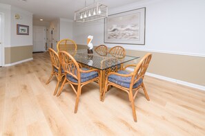 A dining area with a glass-top table surrounded by wicker chairs with blue cushions. - 2BR Oceanfront Condo with Elevator and Shared Pool! South Shores II 203 (Surfside Beach)