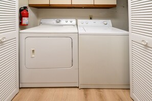 A laundry room with two stacked washers and dryers, a fire extinguisher, and wooden cabinets above. - 2BR Oceanfront Condo with Elevator and Shared Pool! South Shores II 203 (Surfside Beach)