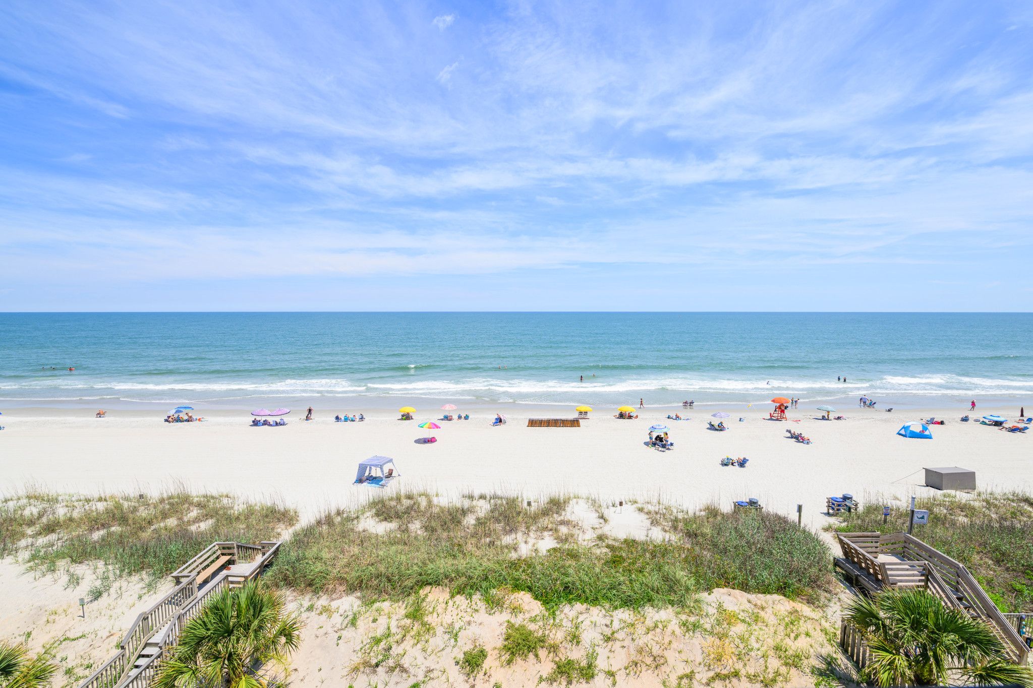A beach with a wooden boardwalk, beach umbrellas, and a sandy shore.