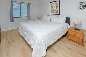 Quarto com cama grande, mesa de cabeceira, luminária e janela com cortinas.