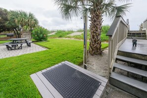 Área externa bem cuidada com mesa de piquenique, palmeira e deck de madeira com escadas.