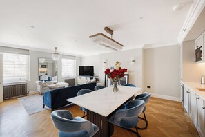 A modern living room with a dining area, a flat-screen TV, and a vase with red flowers. - Spacious 1-Bed in the Heart of Marylebone, London (London)