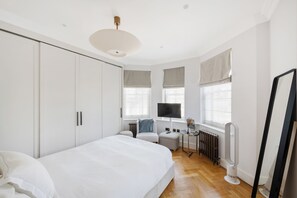 A modern bedroom with a bed, a desk, a chair, a TV, and a radiator. - Spacious 1-Bed in the Heart of Marylebone, London (London)