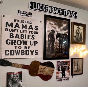 Eine Wand mit verschiedenen Erinnerungsstücken, darunter eine Gitarre, gerahmte Bilder und ein Schild mit der Aufschrift 'LUCKENBACH TEXAS'.