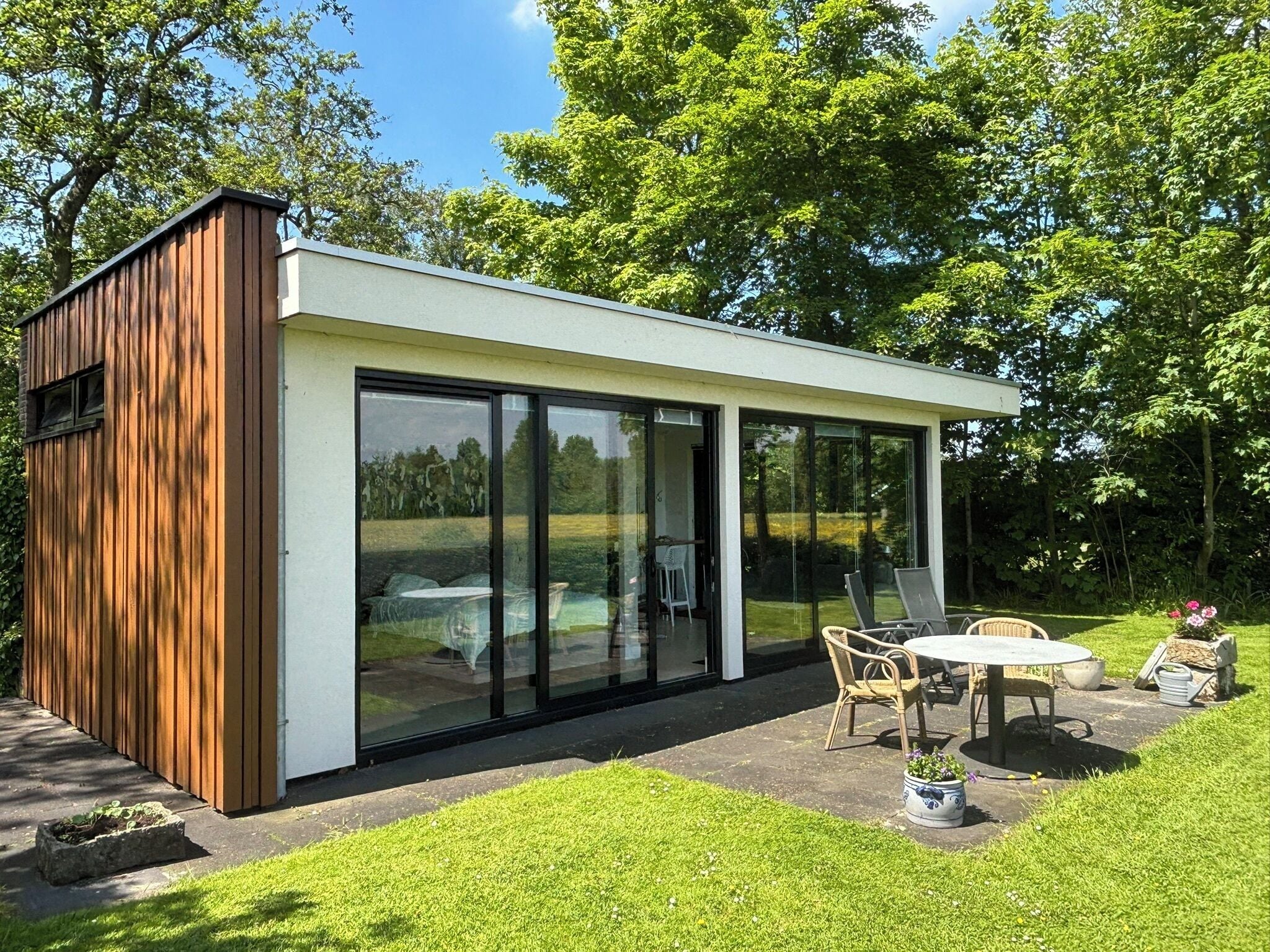 Una estructura moderna al aire libre con cerramiento de vidrio, revestimiento de madera y zona de estar con mesa y sillas.