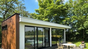 Een moderne buitenconstructie met glazen wanden, een houten gevel en een zithoek met een tafel en stoelen.