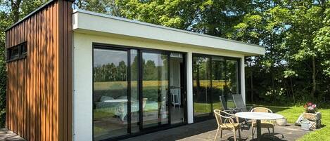 A modern outdoor structure with a glass enclosure, a wooden exterior, and a seating area with a table and chairs.