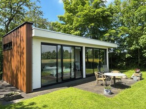 Eine moderne, offene Struktur mit Glasfassade, Holzaußenverkleidung und einer Sitzgruppe mit Tisch und Stühlen.