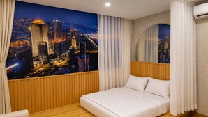 Ett hotellrum med en säng, träpanel på väggarna, utsikt över staden och ett stort fönster med gardiner.