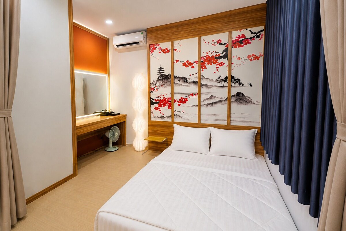 Ein Hotelzimmer mit Bett, Nachttisch, Klimaanlage, Wandbild und Vorhängen.