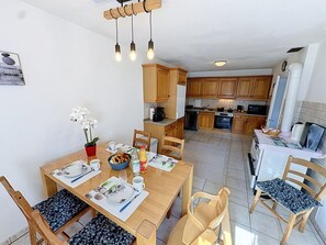 Et moderne køkken med træskabe, et spiseområde med et bord dækket til to og en opholdsstue med sofa og fjernsyn.